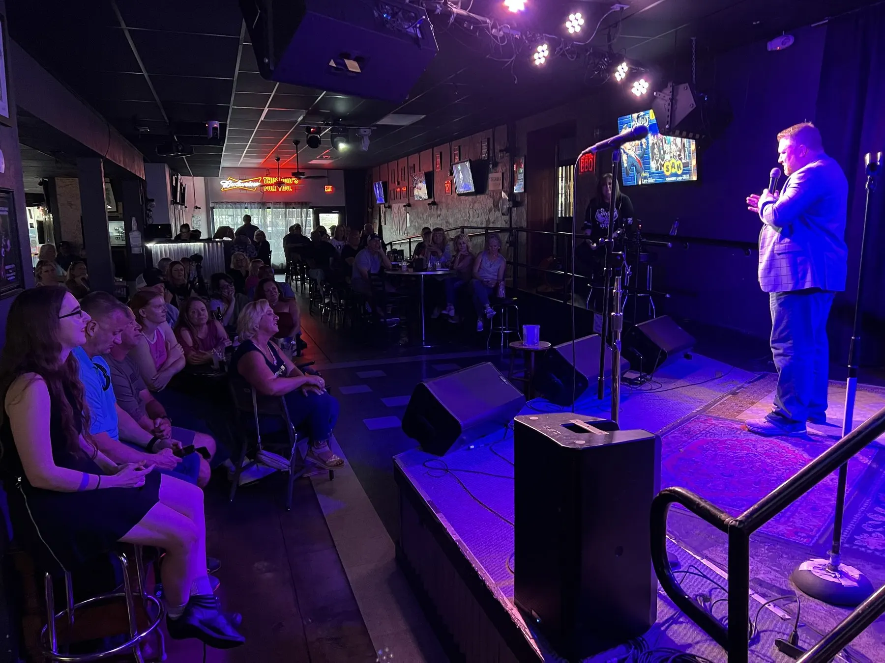 A comedian performing on stage at The Alley in Sanford in front of a seated crowd, May 2025.